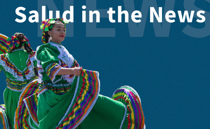 Two Latina women, wearing colorful traditional Mexican dresses, dancing with words "Salud in the News" behind their image.