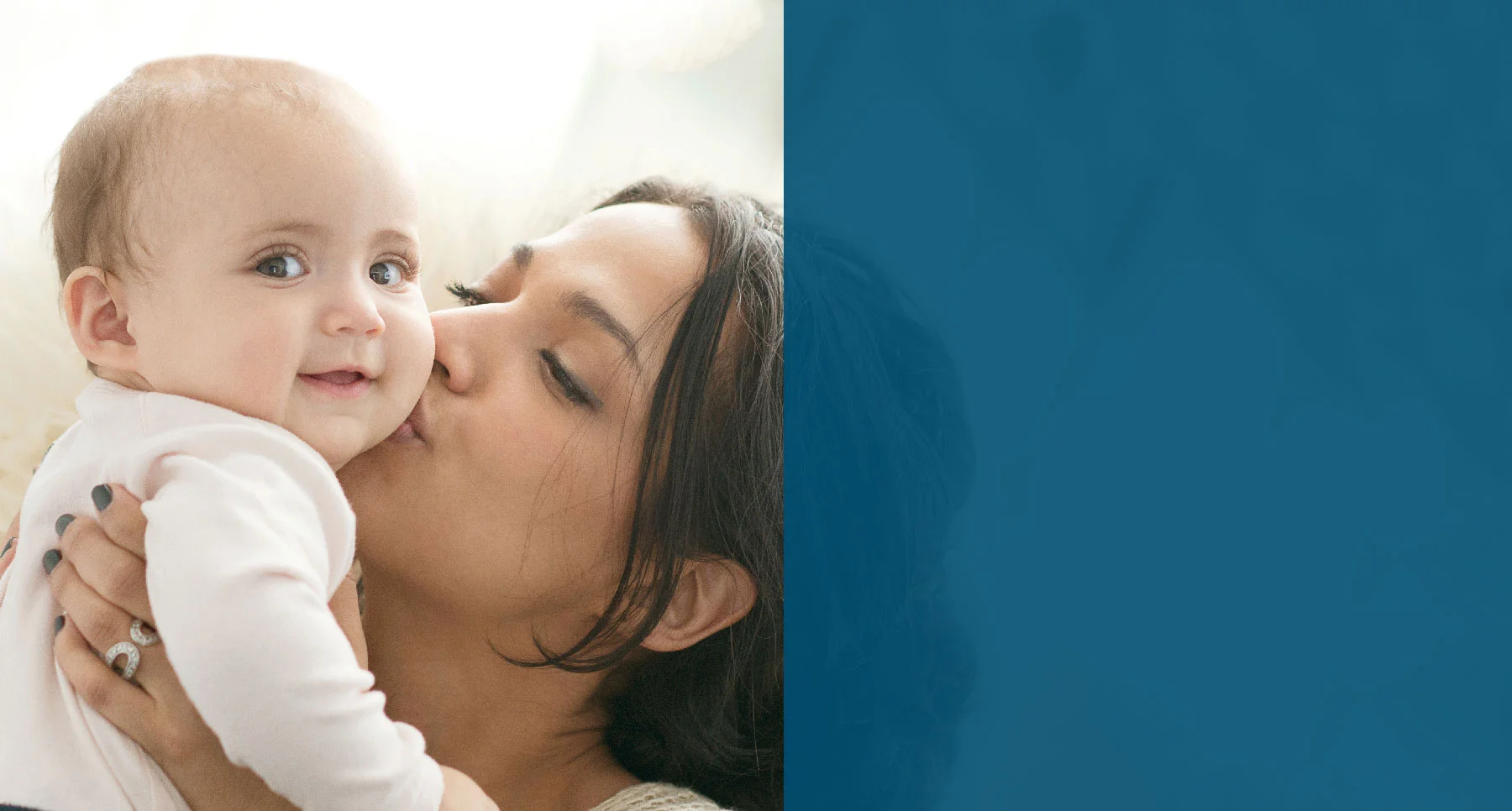 Young mother holding smiling baby and kissing it on the cheek